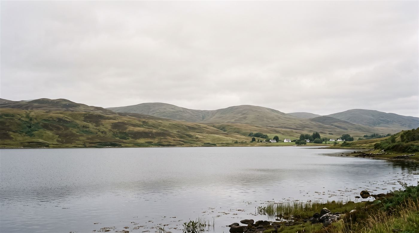 A quiet Highland loch beneath soft green hills and a light overcast sky — the calm of the Highlands.